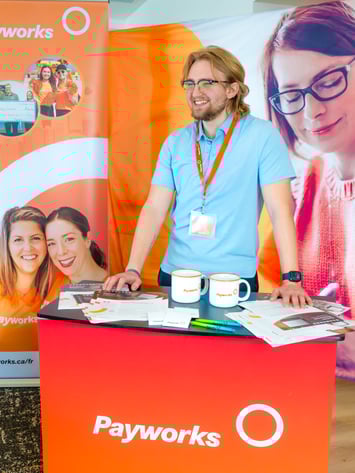 A Payworks employee smiles while standing behind a Payworks-branded tradeshow booth. 