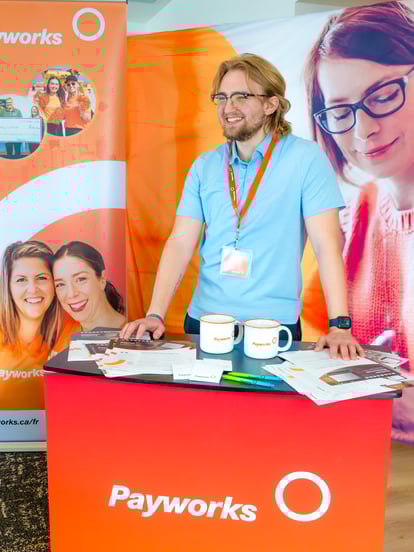 A Payworks employee smiles while standing behind a Payworks-branded tradeshow booth. 