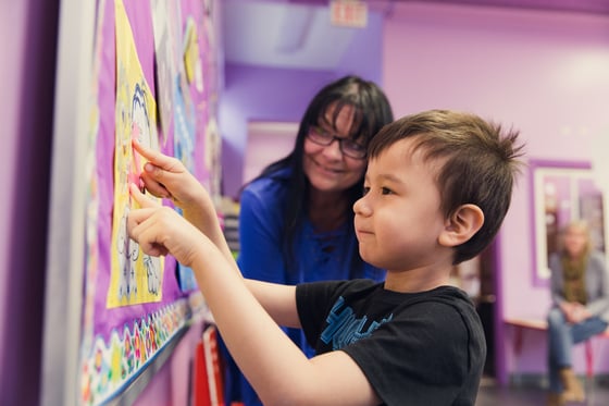An adult and a small child looking at a bulletin board with a photo on it. 