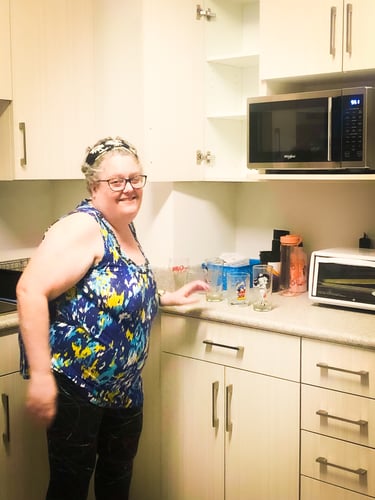 A tenant unpacking drinking glasses into a tall white kitchen cabinet.
