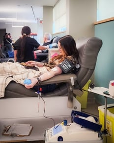 A Payworks staff sitting in a large chair donating blood while looking at their phone.