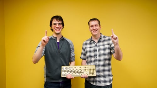 Two Payworks staff holding a gold keyboard and holding up their hands to signify they are number one. 