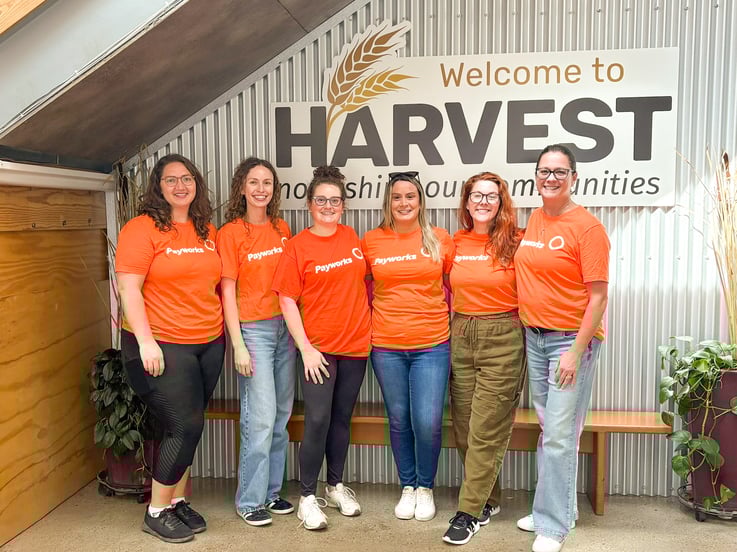 Six personnes en chandail orange Payworks sourient pour la photo devant une enseigne Harvest Manitoba.