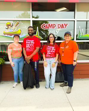 Payworks volunteers smiling in front of the Camp Day sign.