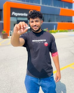 Un membre du personnel se tient devant le bureau de Payworks et brandit un badge de don du sang portant le chiffre « 1 ».