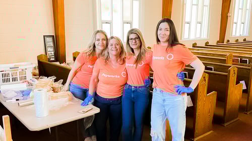 Quatre employés de Payworks debout dans une église devant une table remplie d’épiceries emballées.