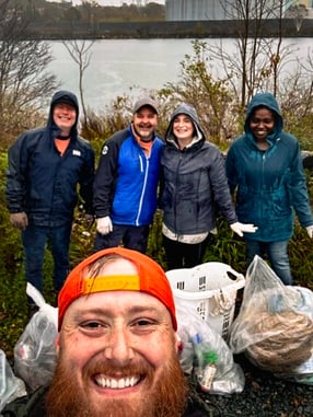 Five Payworks employees in rain gear holding garbage bags at the beach. 