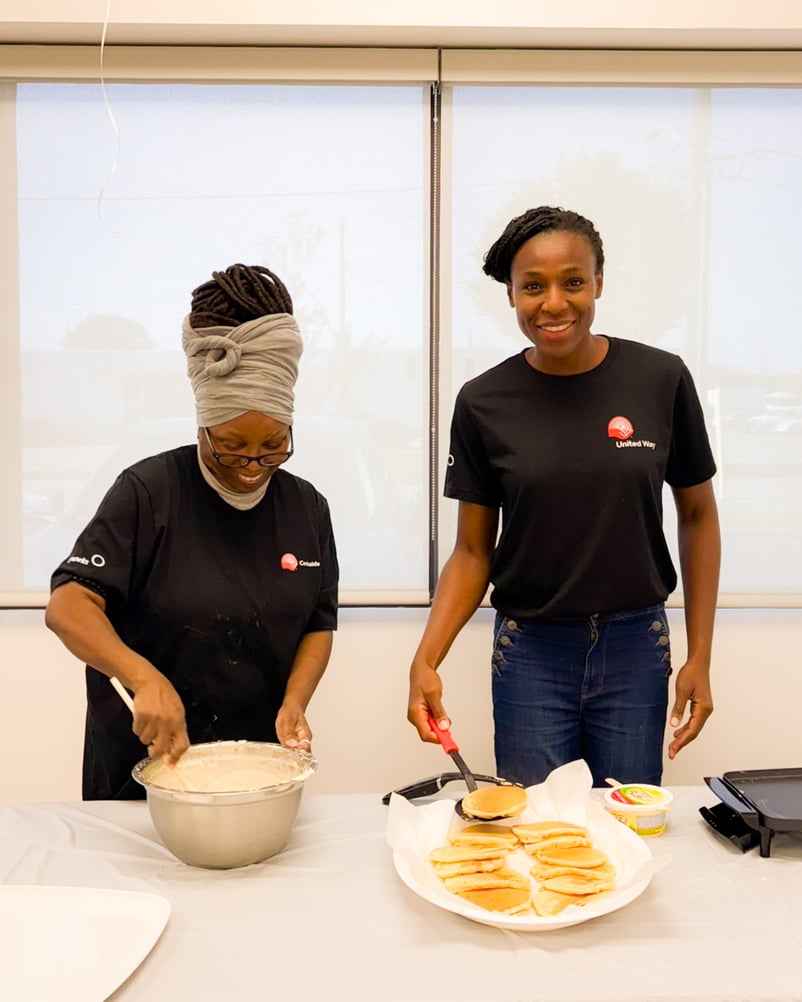 Deux personnes qui portent des chandails du comité Centraide de Payworks mélangent de la pâte à crêpes et font cuire des crêpes.