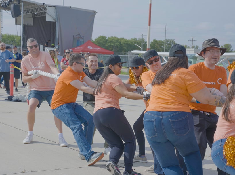 Un groupe de personnes qui portent des chandails orange tire une longue corde blanche. 