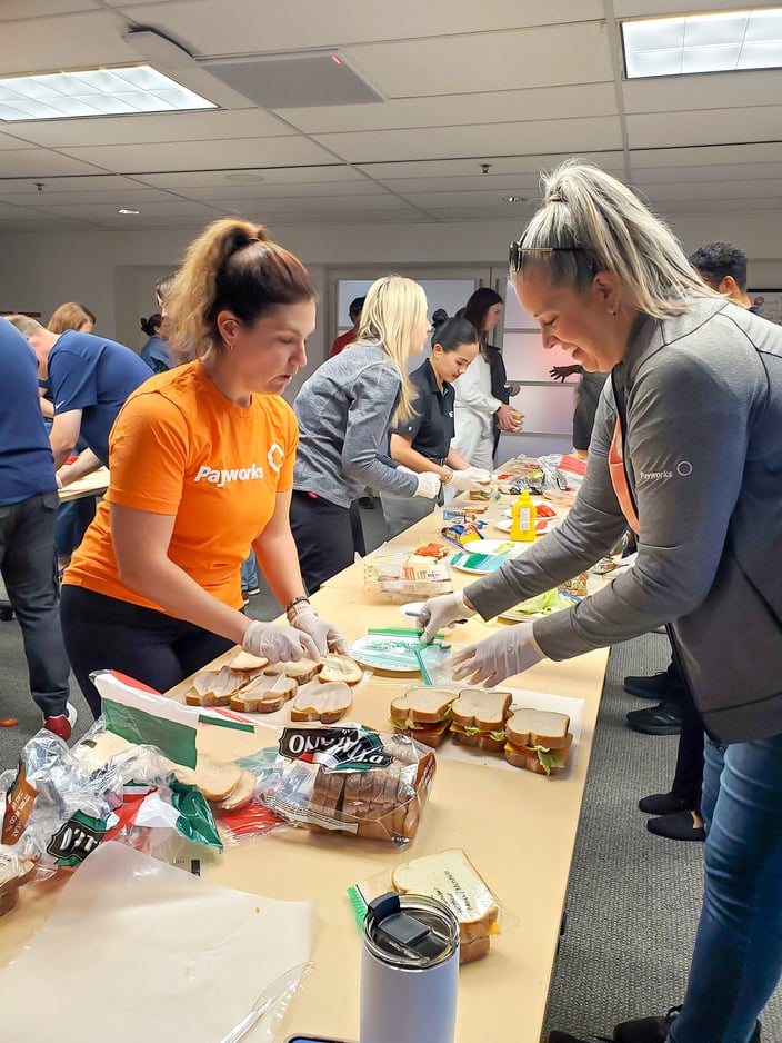 Un groupe de personnes en train d’assembler des sandwiches à de longues tables.