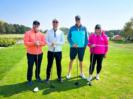 Four Payworks staff members posing for a photo with their golf clubs on a tee box. 