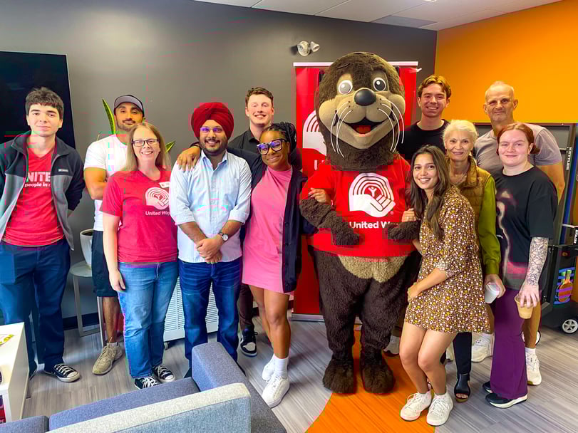 Un groupe de personnes dans un bureau debout avec une mascotte de Centraide. 