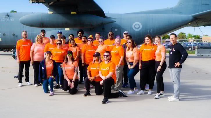 L’équipe de Payworks, vêtue de chandails orange, debout devant un avion lors de l’événement de remorquage d’avion de Centraide Winnipeg en 2024.