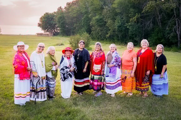 10 women standing side by side in a field. 