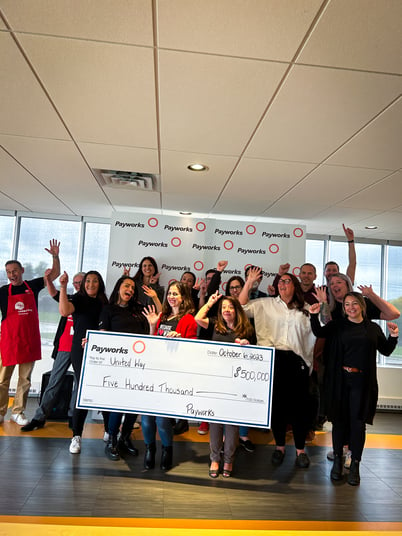 Sixteen Payworks staff cheering around a giant cheque for $500,000. 