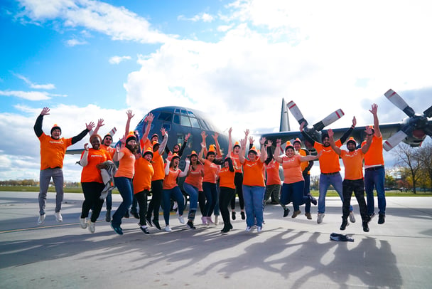 20 Payworks staff jumping in front of a giant plane.