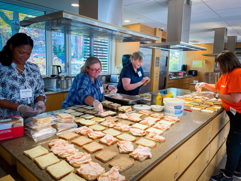 Four Payworks staff members surround a large island full of sandwiches they are putting together. 