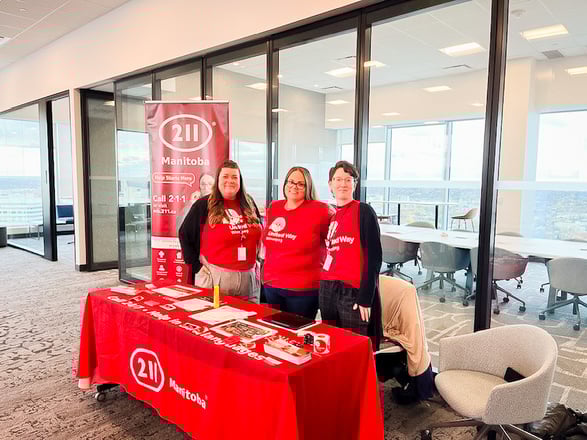 Trois partenaires de campagne parrainée Centraide sont assis à une table d’information, entourés d’affiches Centraide 211.