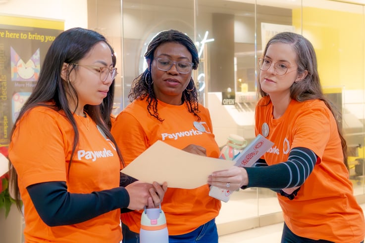 Trois personnes en chandail orange Payworks consultent le contenu d’une chemise de classement.