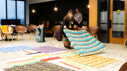 A Blanket Exercise facilitator laying a blanket down in an open space on top of several other blankets spread out across the ground.