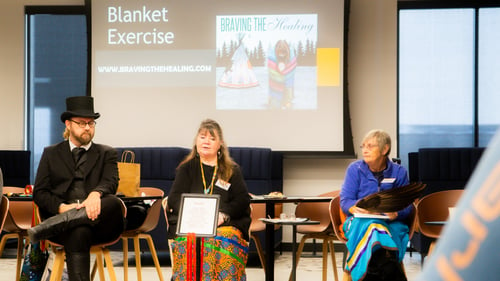 Three Blanket Exercise facilitators seated in a row and addressing the circle.