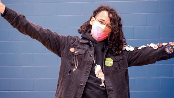 An individual wearing a mask with a vaccination sticker, holding their arms out in celebration.