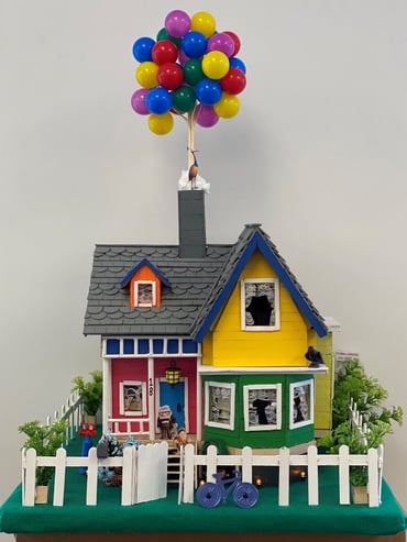 Popsicle stick house with balloons coming out of chimney. 