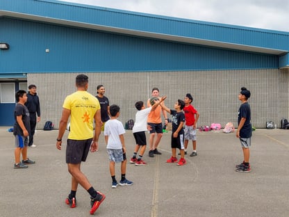 Three adults and seven children playing basketball on an outdoor court. 