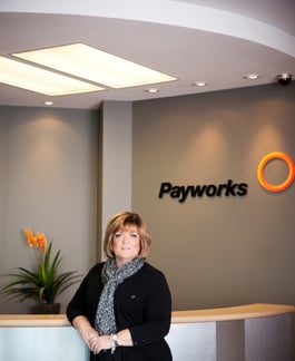 Payworks Co-Founder Barb Gamey standing at a reception desk with a Payworks logo on the wall behind her.