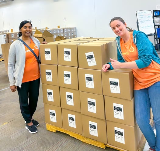 Deux personnes en chandail orange Payworks se tiennent près de cartons de lentilles empilés.