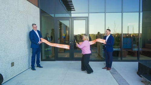 -	Two Payworks staff holding an orange ribbon while a third staff member cuts the ribbon with oversized gold scissors..