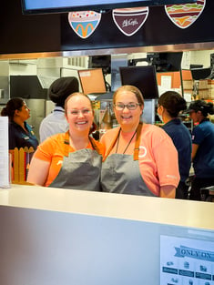 Two staff members in matching orange t-shirts behind a fast food counter.