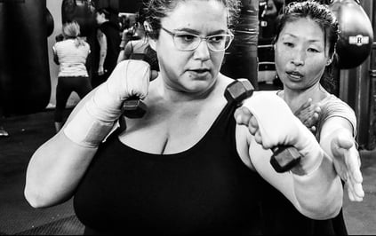 One female punching with weights in her hand. Another female is helping her.