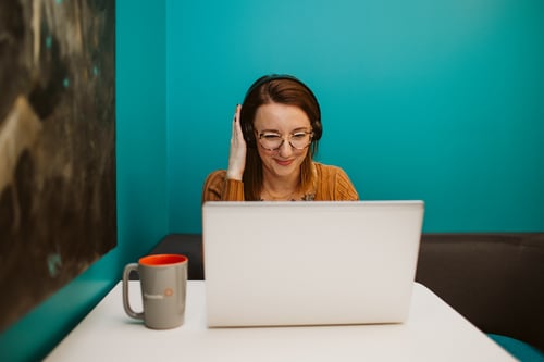 A Payworks employee smiles at her laptop while wearing a phone headset.