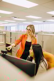 Two Service staff looking at and discussing what’s shown on the computer monitor of the staff member who is seated. 