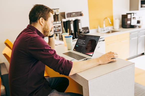 A person seated at a kitchen counter works on a laptop with the Payworks website visible on the screen.