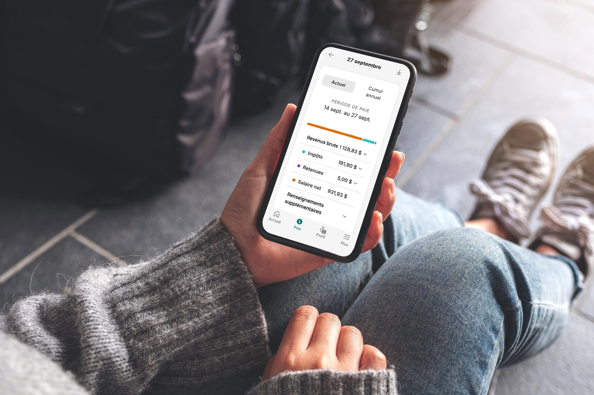 Femme assise sur le sol, consulte son dernier bulletin de paie sur l’application Libre-service de Payworks.
