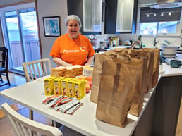 Rachel Wolman, rédactrice technique chez Payworks, dans sa cuisine, portant un filet à cheveux. Des sacs en papier et de la nourriture se trouvent sur le plan de travail face à elle. 