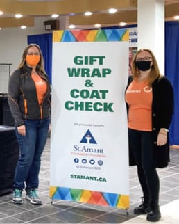 Two Payworks staff standing beside a sign that says, "gift wrap and coat check".