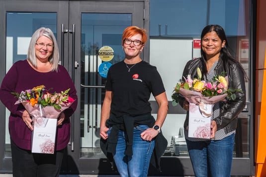 Trois employés Payworks, dont deux tenant des bouquets de fleurs.