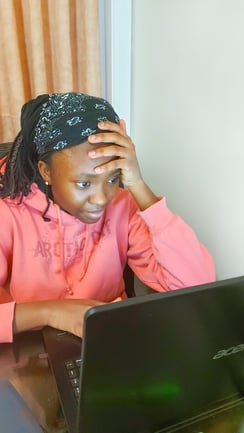 A university student sits at a table, looking at a laptop screen.