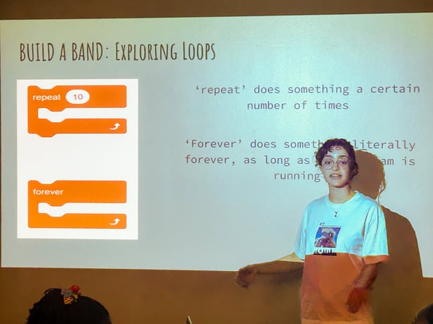Une instructrice devant un écran expliquant le codage de boucles infinies et de répétition.