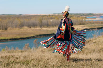 An Indigenous person dancing in a prairie landscape.