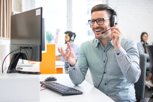 Un employé portant un casque d’écoute, souriant devant son ordinateur, lors d’une réunion virtuelle.
