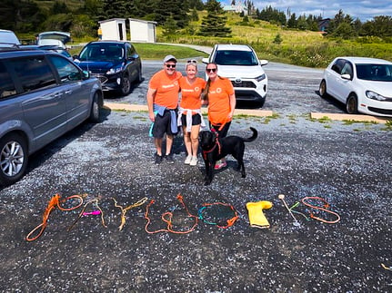 Trois employés de Payworks et un chien se tiennent devant l’inscription « Payworks » qui a été tracée dans le sable. 