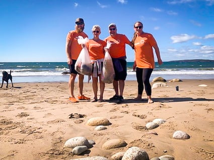 Quatre membres du personnel de Payworks sont sur une plage, des sacs poubelles à la main.