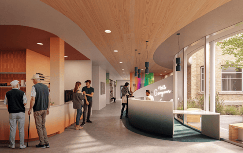 A wide hallway filled with natural light, a welcome desk, and people socializing.