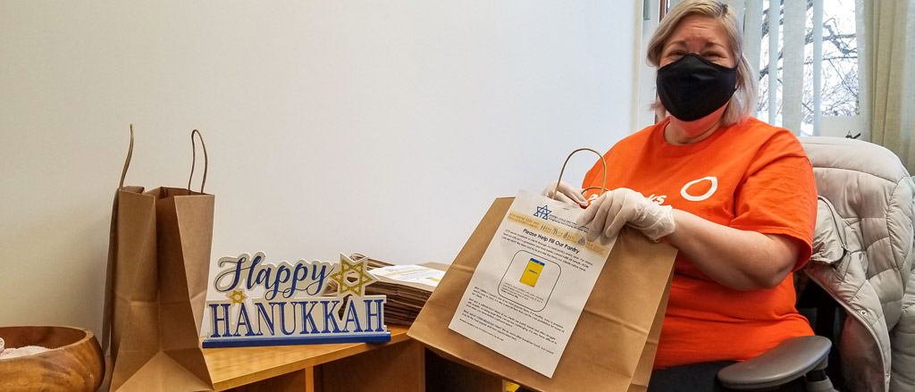 Payworks Technical Writer Rachel Wolman standing in her kitchen wearing a hair net. There are several kraft paper lunch bags on the counter with lunch items such as sandwiches and juice boxes.  