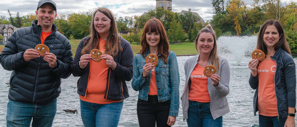 Cinq employés de Payworks portant des t-shirts orange assortis, brandissant des biscuits sourire.