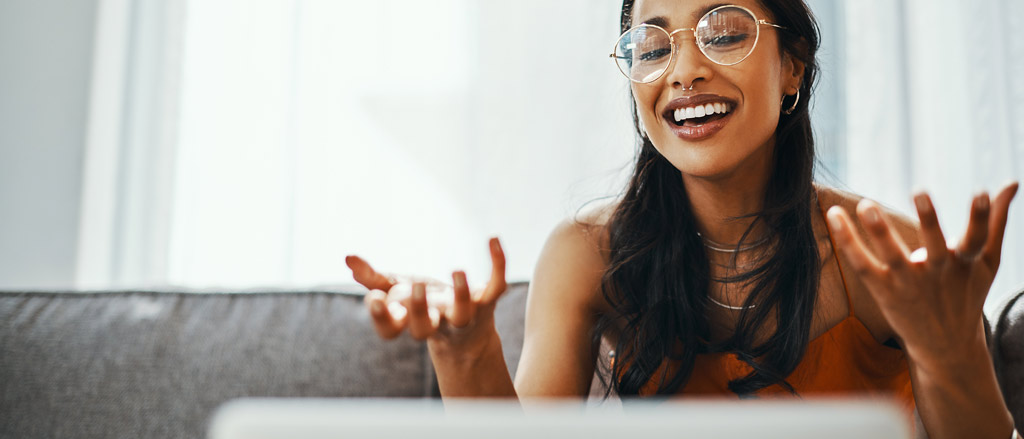 Une femme est assise sur un canapé dans son salon. Elle regarde son ordinateur portable et parle en bougeant ses mains. On voit le texte « Comment diriger une équipe dans un environnement virtuel ». 